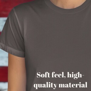 K&ouml;nnte beinhalten: Nahaufnahme eines dunkelgrauen T-Shirts. Das Shirt hat kurze &Auml;rmel und einen Rundhalsausschnitt. Der Text "Soft feel, high-quality material" ist in Wei&szlig; auf dem unteren Teil des Shirts aufgedruckt.