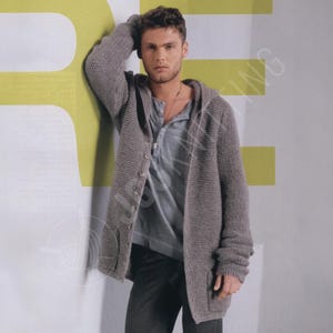 May include: A gray hooded cardigan with a button-up front and pockets. The long-sleeved sweater is made of a thick knit material. The person in the image is wearing a gray Henley shirt and dark pants.