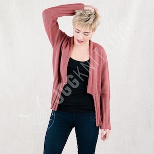 May include: A dusty rose-colored cardigan with a draped front and ribbed sleeves. The open-front sweater is worn over a black tank top and dark blue jeans. The sleeves have a flared design.