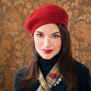 May include: A red knitted beret. The beret is worn by a person wearing a navy blue turtleneck sweater. A plaid scarf with a red heart pin and a necklace with clear stones is also visible.