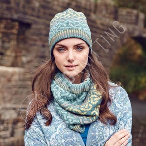 May include: A teal knit hat and cowl set with a geometric pattern in yellow and light blue. The hat has a folded brim and the cowl is a circular scarf. The woman in the image is wearing a blue patterned jacket.