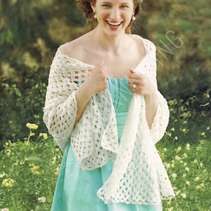 Puede incluir: Un chal de crochet crema de tejido abierto drapeado sobre un vestido azul claro. El chal tiene un delicado patrón de encaje y se lleva sobre los hombros. El fondo presenta follaje verde y flores amarillas.