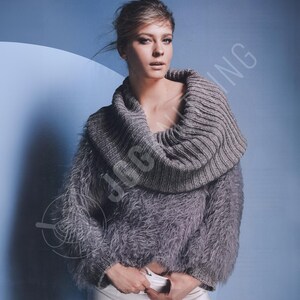 Puede incluir: Un suéter gris con un cuello alto y acanalado y mangas esponjosas y texturizadas. El suéter es de color gris apagado y tiene un diseño único y elegante. El fondo es azul claro.