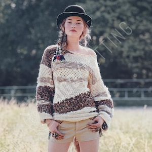 May include: A knitted off-the-shoulder sweater in cream, brown, and beige stripes. The sweater has a loose fit with long sleeves and a textured knit design. The model is wearing a black hat and tan shorts.