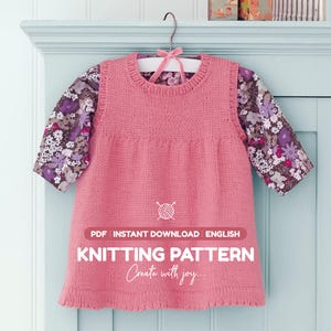 Könnte beinhalten: Ein rosa gestricktes ärmelloses Kleid mit Rundhalsausschnitt, getragen über einem langärmeligen Oberteil mit violett-weißem Blumenmuster. Das Bild enthält den Text: PDF INSTANT DOWNLOAD ENGLISH KNITTING PATTERN Create with joy.
