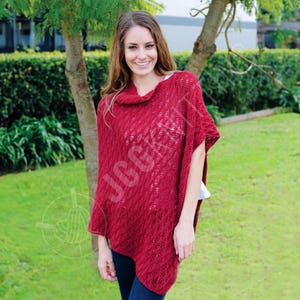 May include: A red knitted poncho with a cowl neck. The poncho has a textured pattern and is worn over a white top and blue jeans. The image is taken outdoors with a green background.