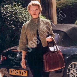 Puede incluir: Una mujer con una chaqueta de punto verde con un solo botón y un bolso a juego. La chaqueta tiene cuello alto y mangas tres cuartos. El bolso es de color marrón oscuro.