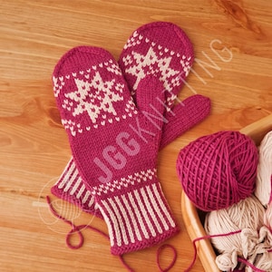 May include: Magenta knitted mittens with white snowflake designs and striped cuffs. A ball of magenta yarn and a wooden basket with yarn are in the background. The mittens are handmade, ideal for winter.