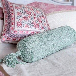 Peut inclure: Un traversin décoratif en tricot vert clair avec un pompon assorti. Un coussin carré avec un motif floral rouge et rose est derrière le traversin. Les coussins sont sur un couvre-lit blanc. Le traversin mesure environ 40 cm de long.
