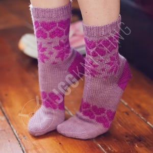 Pode incluir: Um par de meias de malha em tons de roxo e magenta. As meias apresentam um padrão floral na perna e no pé, com calcanhares e dedos magenta sólidos. As meias são exibidas em uma superfície de madeira.