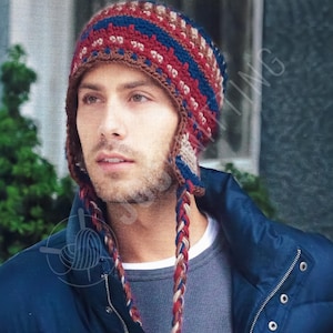 May include: A crocheted hat with ear flaps and braided ties. The hat features a pattern of red, blue, and brown colours. The ear flaps and ties are brown, red, and blue. The hat is worn by a person.