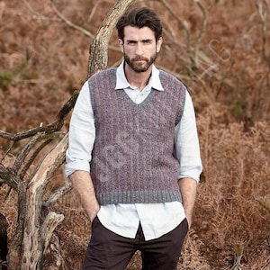 Puede incluir: Un chaleco de punto gris y rojo con un patrón, con cuello en V. Se lleva sobre una camisa azul claro. La persona está de pie al aire libre con las manos en los bolsillos.