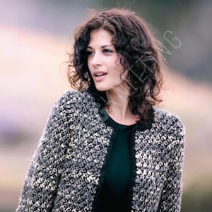 May include: A woman wearing a gray, black, and white tweed jacket with a black trim. The jacket is open, revealing a dark green top. The woman has curly brown hair.