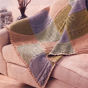 May include: A patchwork knitted blanket in shades of pink, green, and purple, draped over a sofa. The blanket features various textured stitch patterns, including cable and bobble designs. The edges are finished with a decorative border.