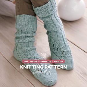 Könnte beinhalten: Ein Paar hellblaue Strickstrümpfe mit geripptem Bündchen und einem strukturierten Blattmuster am Fuß. Das Bild enthält den Text: PDF INSTANT DOWNLOAD ENGLISH KNITTING PATTERN Create with joy.