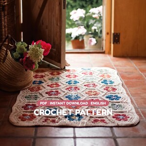 Op de afbeelding: Een rechthoekig gehaakt kleed met een herhalend bloemmotief in tinten rood, blauw en groen op een crèmekleurige achtergrond. De tekst luidt: PDF INSTANT DOWNLOAD ENGLISH CROCHET PATTERN Create with joy. Een gevlochten mand met bloemen staat ernaast.