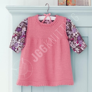 May include: A pink knitted dress with a round neckline and a ruffled hem, layered over a floral print long-sleeved shirt. The dress is hanging on a white hanger with a pink bow.