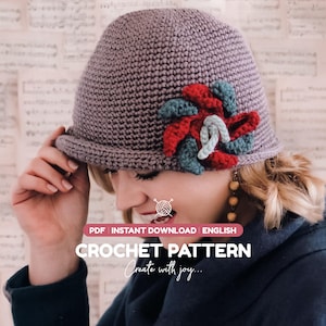Peut inclure: Un patron de crochet PDF pour un chapeau cloche mauve avec une fleur décorative rouge, bleu sarcelle et bleu clair. Le texte sur l'image indique : PDF INSTANT DOWNLOAD ENGLISH CROCHET PATTERN Create with joy. Le chapeau a un bord roulé.