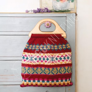 Könnte beinhalten: Eine gestrickte Tasche mit Holzgriff und dekorativer Blume. Die Tasche ist überwiegend rot mit bunten geometrischen Mustern in Türkis, Gelb, Rosa und Weiß. Der Griff ist aus hellem Holz.