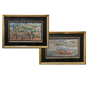 May include: Two rectangular framed paintings featuring detailed scenes with figures, landscapes, and structures. Each artwork is enclosed in a black mat and a gold-toned frame. The left painting depicts a procession, while the right shows a boat.