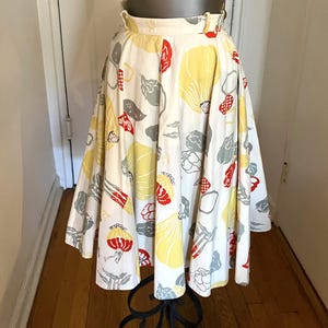 May include: A vintage, full skirt with a high waist, displayed on a mannequin. The skirt features a white background with a repeating pattern of yellow, red, and gray floral and abstract shapes. The skirt is knee-length and has a wide waistband.