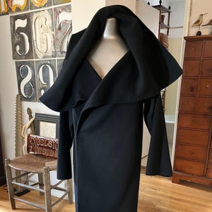 May include: A long, black coat with a dramatic, oversized collar. The coat is displayed on a mannequin, showcasing its flowing design and elegant silhouette. The coat's length extends to the ankles, and the sleeves are long.