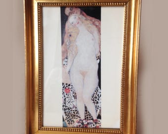 May include: A rectangular gold-toned frame with a beaded inner border containing a vertical print of a pale figure with long blonde hair standing in front of a darker figure, with a leopard print pattern and floral accents at the bottom edge.