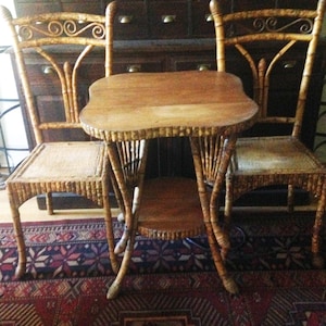May include: A set consisting of two chairs and a small table, all constructed from light brown bamboo with a natural finish. The chairs feature woven seats and curved backrests, while the table has a square top and a lower circular shelf.