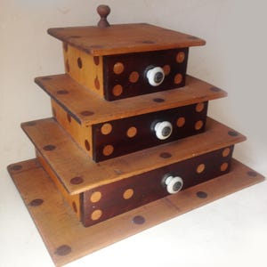 May include: A tiered wooden storage box set with a natural wood finish and dark brown polka dots. Each box has a white knob and a lid. The boxes are stacked on top of each other.