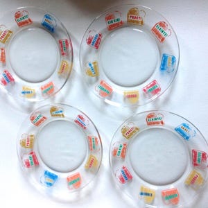 May include: Four clear glass plates featuring a circular pattern of colorful beer mug graphics. Each mug contains text in various languages including Slainte, Prost, Cin Cin, and Skal, printed in red, blue, yellow, and orange ink around the rim.