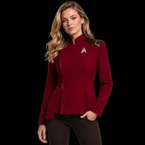 Può includere: Una giacca a maniche lunghe rosso scuro con chiusura a zip asimmetrica, colletto alto e un'insegna metallica delta di Starfleet sul petto sinistro. Il capo presenta dettagli marrone scuro sulle spalle e un orlo a baschina strutturato.