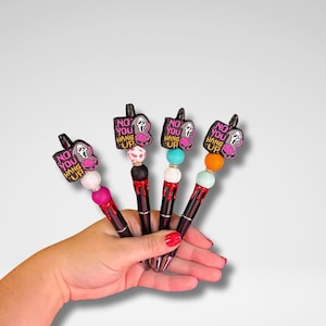 May include: Four black pens with decorative toppers featuring a Ghostface mask and the text "NO YOU HANG UP". Each pen has a different colored bead and a red, black, or white accent.