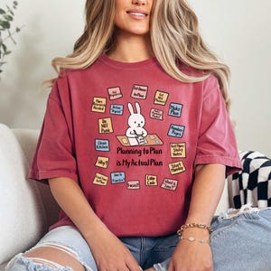 May include: A maroon t-shirt with the text "Planning to Plan is My Actual Plan" and a cartoon rabbit. The shirt has various sticky notes with planning-related phrases like "Make Plan" and "Start Monday."