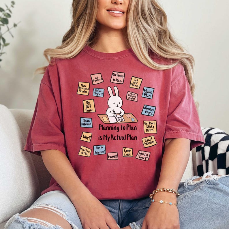 May include: A maroon t-shirt with the text "Planning to Plan is My Actual Plan" and a cartoon rabbit. The shirt has various sticky notes with planning-related phrases like "Make Plan" and "Start Monday."