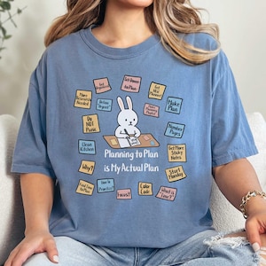 May include: A light blue t-shirt with the text "Planning to Plan is My Actual Plan" and a cartoon bunny surrounded by sticky notes. The sticky notes have phrases like "Make Plan" and "Start Monday".