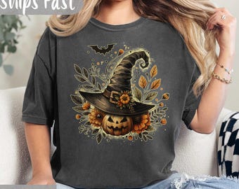 May include: Dark gray t-shirt featuring a Halloween design. The graphic includes a witch's hat, a carved pumpkin, and autumn leaves. The text "Ships Fast" is at the top, and "Pepper" is at the bottom.