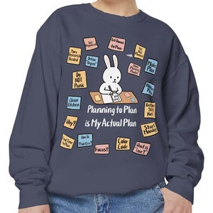 May include: Navy blue sweatshirt featuring a cartoon bunny at a desk with the text "Planning to Plan is My Actual Plan." Surrounding the bunny are sticky notes with phrases like "Make Plan" and "Do Not Panic."