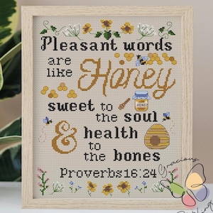 Może przedstawiać: Haftowane obrazki wykonane techniką krzyżykową na beżowym tle z cytatem o tym, że miłe słowa są jak miód, słodkie dla duszy i zdrowe dla kości. Cytat pochodzi z Księgi Przysłów 16:24. Haftowane obrazki są oprawione w jasną drewnianą ramę.