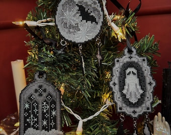 Puede incluir: Adornos navideños de punto de cruz en blanco y negro colgados de un pequeño árbol. Los adornos presentan un murciélago, un fantasma y un diseño de ventana gótica. Cada adorno tiene una cinta negra para colgar y abalorios decorativos.