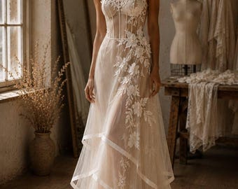 May include: A strapless floor-length gown in a light beige hue, featuring a structured corset-style bodice with visible boning, layered tulle skirt panels, and intricate white floral lace appliques cascading down the side and bodice.