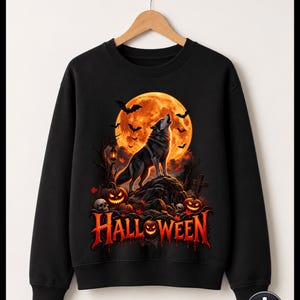 Op de afbeelding: Een zwart sweatshirt met ronde hals en een grafische print van een wolf die naar een grote oranje volle maan huilt. Het ontwerp bevat vliegende vleermuizen, kale bomen, gloeiende pompoenen, schedels en het woord HALLOWEEN in oranje letters.