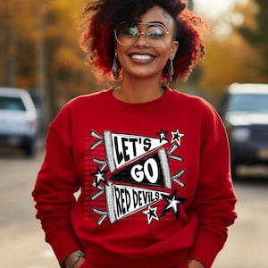May include: A red sweatshirt with the text "LET'S GO RED DEVILS" in a black and white design. The sweatshirt has a crew neck and long sleeves. The design includes stars and banner elements.