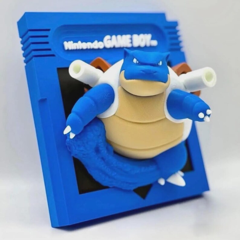 May include: A blue and white 3D printed figurine of a Pokemon character, Snorlax, inside a blue Game Boy cartridge case. The case has the text "Nintendo GAME BOY" on the front.