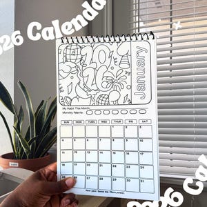 May include: A white 2026 calendar with a black wire binding. The January page features a doodle-style design with the number 26. The calendar includes a habit tracker and the text "New year. Same me. More power."