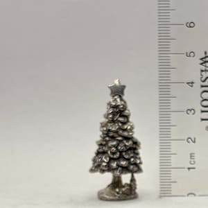 May include: A small, silver-colored Christmas tree figurine with a star on top. The tree is approximately 2 inches tall. The tree has a textured surface and sits on a small base.