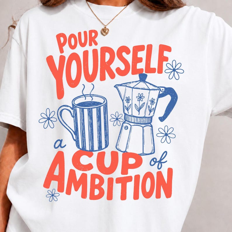 K&ouml;nnte beinhalten: Ein wei&szlig;es T-Shirt mit einem Grafikdruck, der den roten Schriftzug "POUR YOURSELF A CUP OF AMBITION" sowie blaue Strichzeichnungen einer gestreiften Kaffeetasse und einer Espressokanne zeigt, erg&auml;nzt durch kleine blaue Blumenmotive.