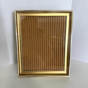 May include: A rectangular picture frame with a metallic gold finish and a textured, beaded outer edge. The frame features a smooth, beveled inner border surrounding a central panel of light brown, vertically corrugated cardboard material.