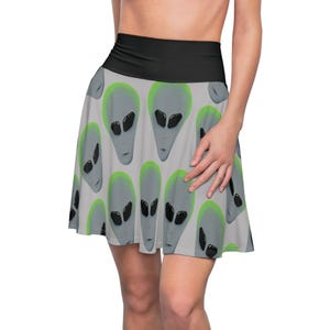 Op de afbeelding: Een skaterrok met een herhaald patroon van grijze aliengezichten met zwarte ogen en groene contouren op een lichtgrijze achtergrond. De rok heeft een brede zwarte tailleband.