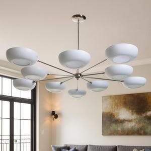 May include: A modern chandelier with multiple white bowl-shaped lights suspended from a central fixture. The lights are arranged in a circular pattern, with a polished metal finish. The chandelier hangs above a living room with a gray sofa and yellow armchair.