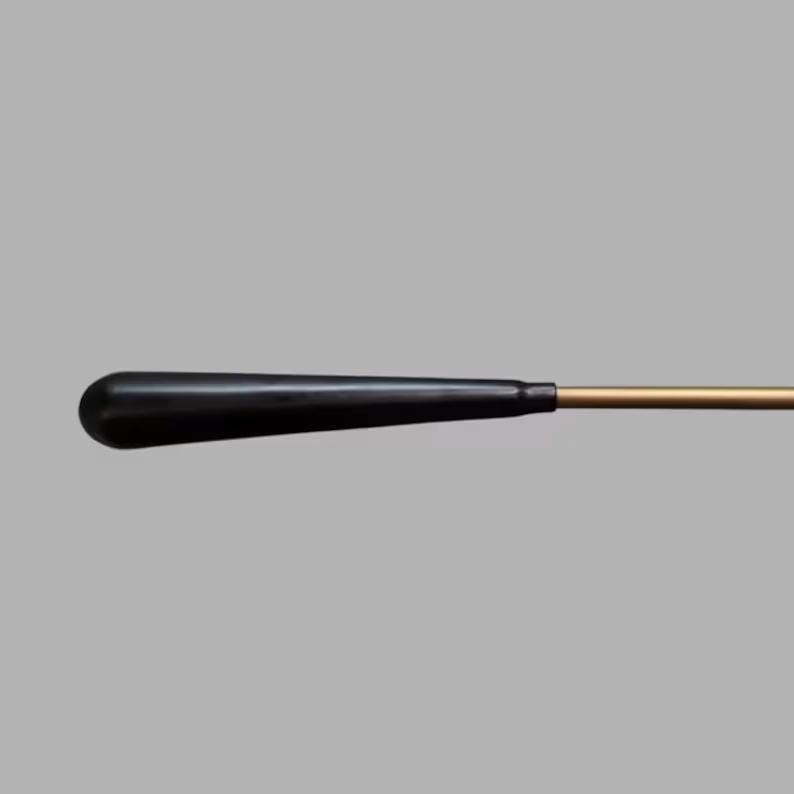 May include: A black conductor's baton with a rounded handle and a thin, gold-colored shaft. The baton is set against a gray background, highlighting its sleek design. This tool is used by conductors to direct musical performances.